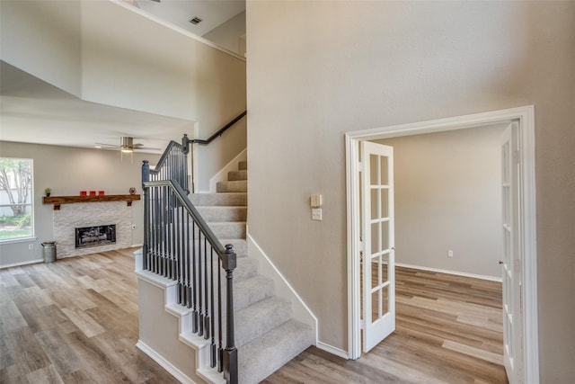 stairs featuring wood-type flooring, ceiling fan, a high ceiling, and a stone fireplace