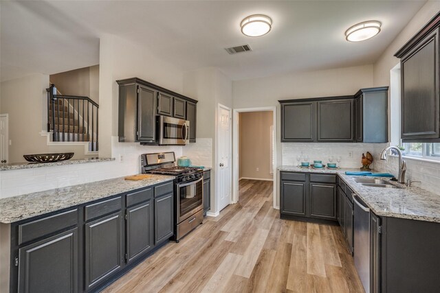 kitchen with light stone counters, sink, tasteful backsplash, light hardwood / wood-style flooring, and stainless steel appliances