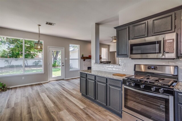 kitchen with light stone countertops, stainless steel appliances, backsplash, and light hardwood / wood-style flooring