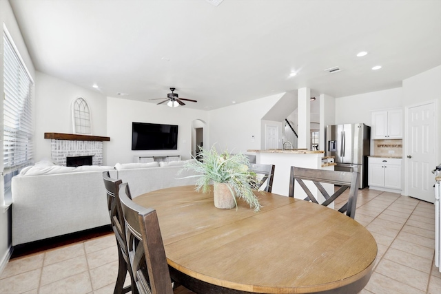 tiled dining room featuring ceiling fan, a fireplace, and sink