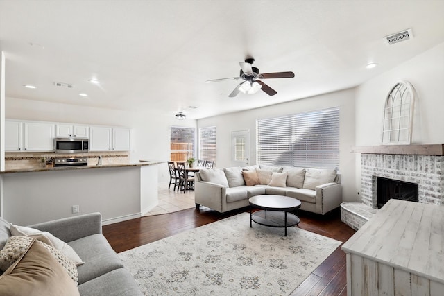 living room featuring a brick fireplace, dark hardwood / wood-style floors, and ceiling fan