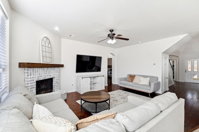 living room with a brick fireplace, dark wood-type flooring, and ceiling fan