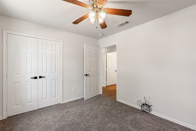 unfurnished bedroom with ceiling fan, dark carpet, and a closet