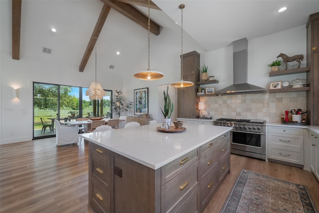 kitchen featuring high vaulted ceiling, hardwood / wood-style flooring, wall chimney exhaust hood, stainless steel range, and tasteful backsplash