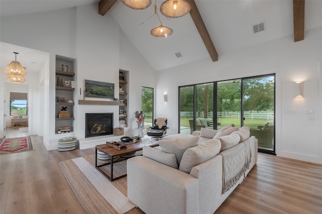 living room with beam ceiling, built in shelves, an inviting chandelier, high vaulted ceiling, and light wood-type flooring