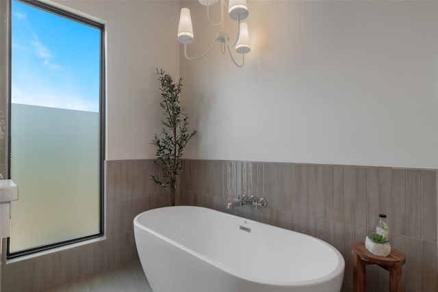 bathroom with a notable chandelier, a tub to relax in, and tile walls