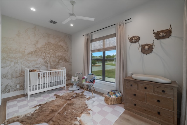 bedroom featuring ceiling fan, light hardwood / wood-style floors, and a crib