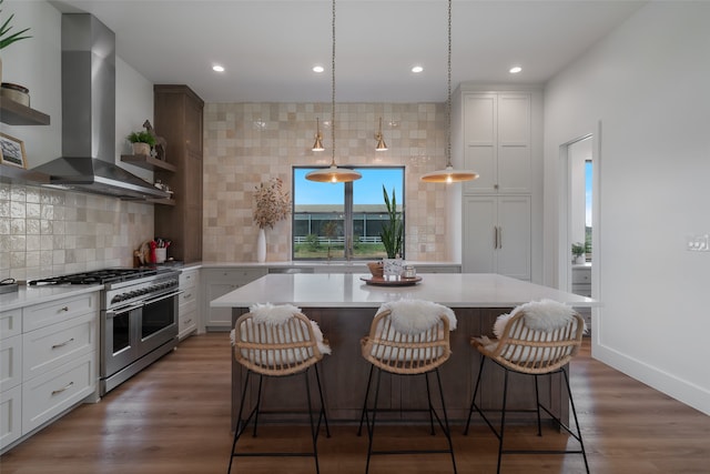 kitchen with tasteful backsplash, wall chimney range hood, range with two ovens, white cabinets, and dark hardwood / wood-style floors