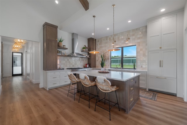 kitchen featuring a breakfast bar, wall chimney exhaust hood, a large island, light hardwood / wood-style floors, and white cabinetry