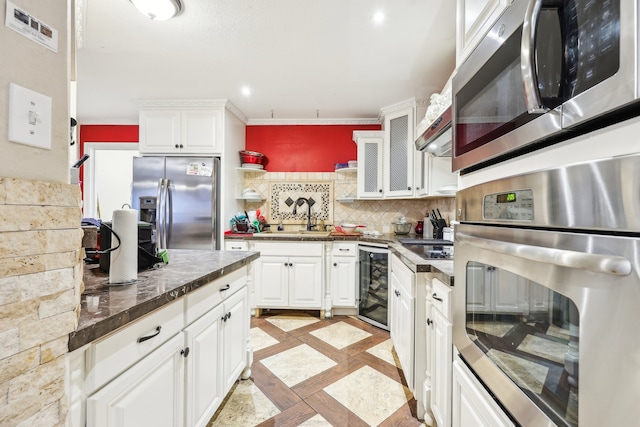 kitchen with wine cooler, appliances with stainless steel finishes, white cabinetry, ornamental molding, and sink