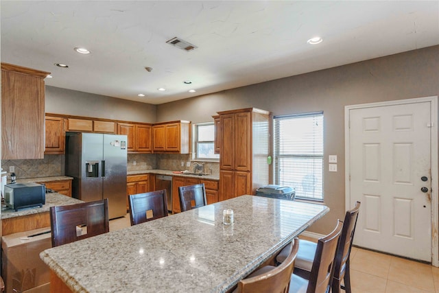 kitchen with a kitchen island, light stone countertops, decorative backsplash, light tile patterned flooring, and appliances with stainless steel finishes