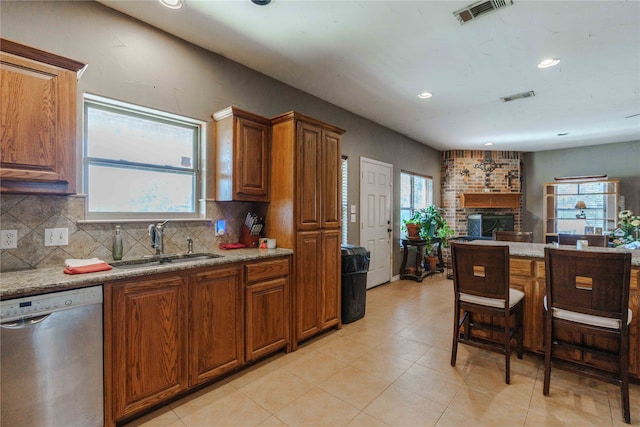 kitchen with a brick fireplace, light stone counters, dishwasher, sink, and backsplash