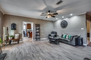 living room with crown molding, wood-type flooring, and ceiling fan