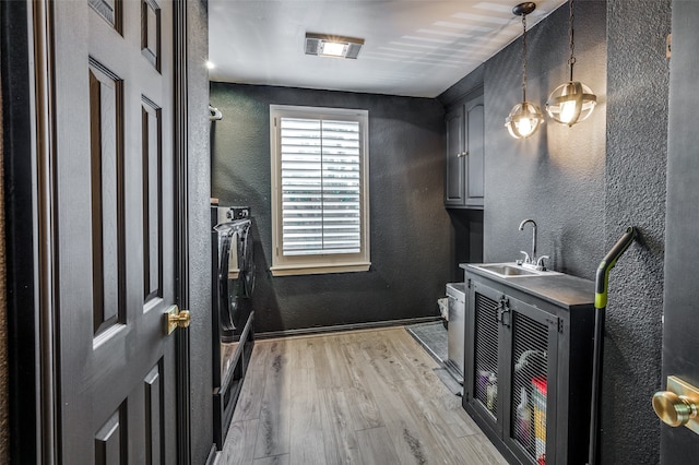 laundry room featuring sink, washing machine and dryer, light hardwood / wood-style flooring, and cabinets