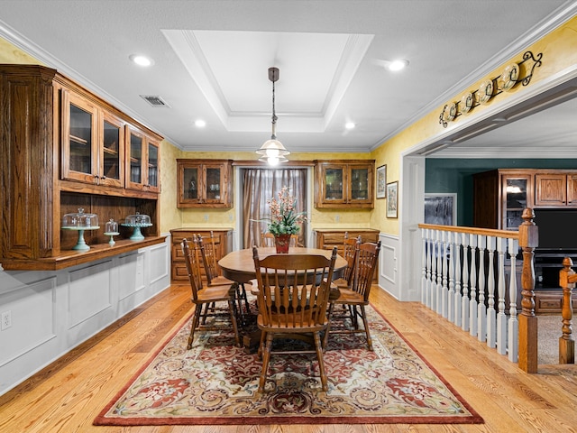 dining space featuring crown molding, a tray ceiling, and light wood-type flooring