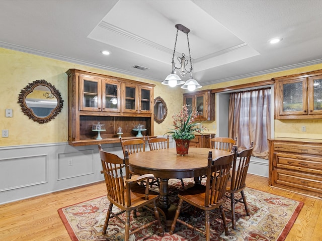 dining space with light hardwood / wood-style flooring, ornamental molding, and a tray ceiling