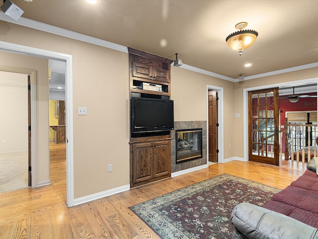 living room featuring french doors, a tiled fireplace, ornamental molding, and light hardwood / wood-style flooring