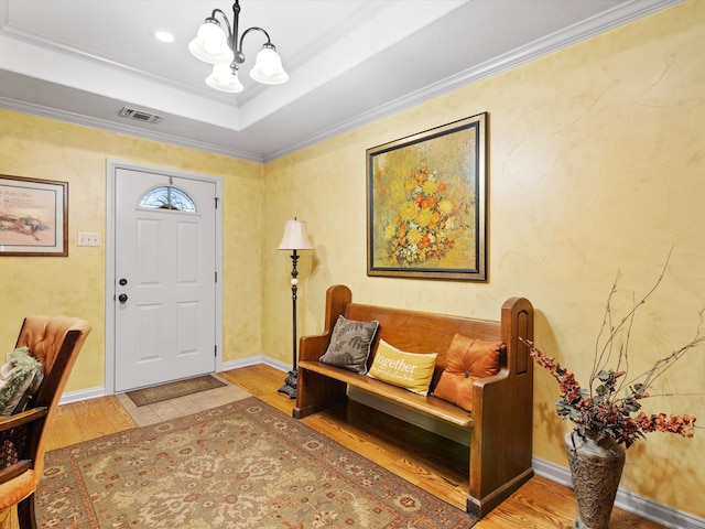 foyer featuring a notable chandelier, ornamental molding, a tray ceiling, and wood-type flooring