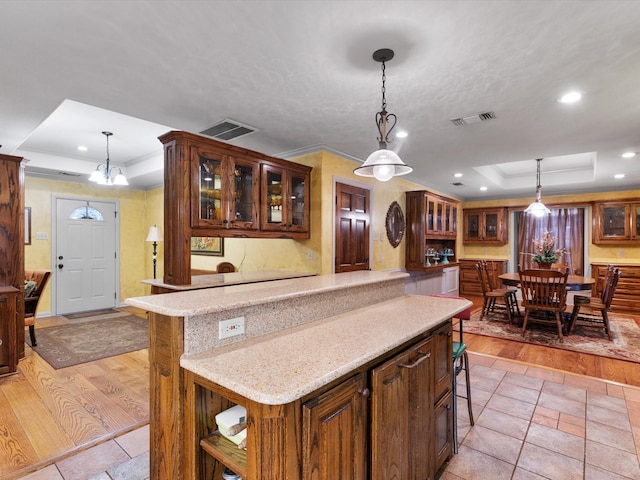 kitchen featuring light hardwood / wood-style flooring, hanging light fixtures, light stone countertops, a kitchen bar, and a raised ceiling