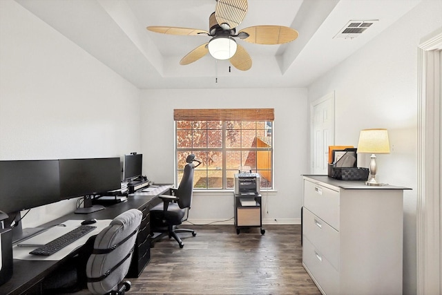 office area with ceiling fan, dark wood-type flooring, and a raised ceiling