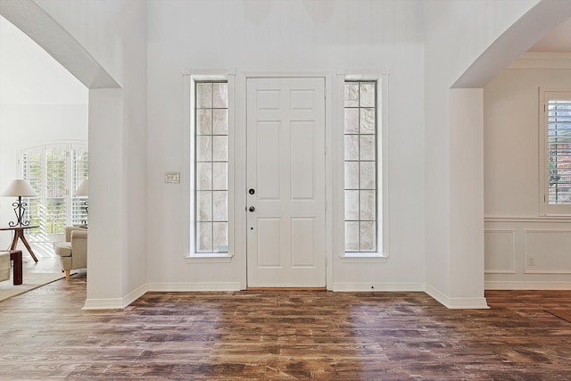 foyer with a wainscoted wall, a decorative wall, wood finished floors, and arched walkways