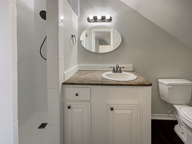 bathroom with toilet, wood-type flooring, tiled shower, vaulted ceiling, and vanity