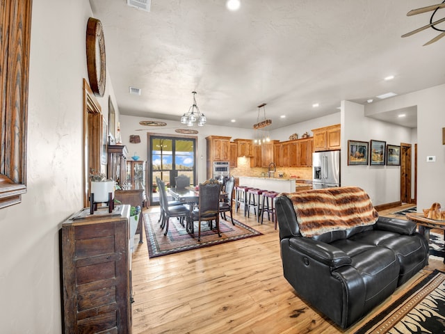 living room with ceiling fan with notable chandelier, light hardwood / wood-style floors, and sink