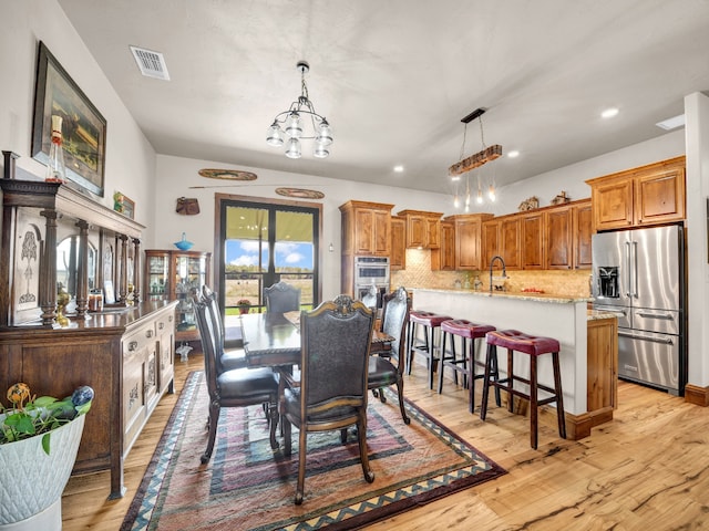 dining area with sink, a notable chandelier, and light wood-type flooring