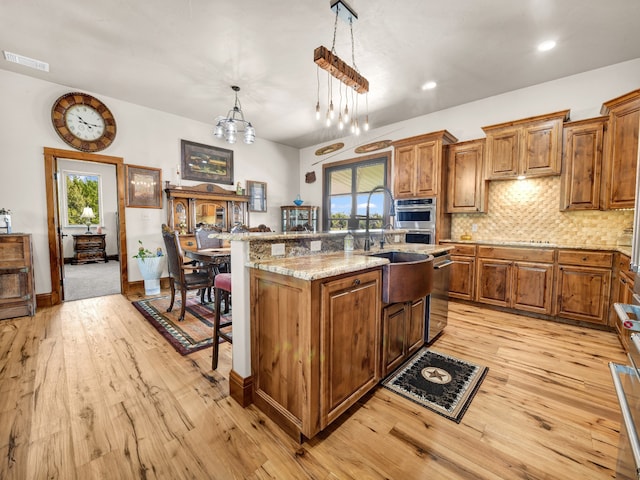 kitchen featuring an inviting chandelier, light stone countertops, an island with sink, decorative light fixtures, and light hardwood / wood-style floors