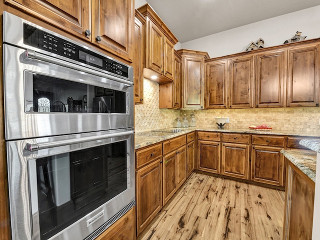 kitchen featuring light stone counters, double oven, backsplash, black electric stovetop, and light wood-type flooring