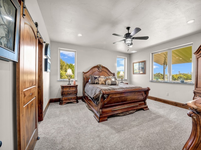 bedroom featuring a barn door, ceiling fan, and light carpet