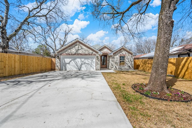 view of front of home featuring an attached garage, fence, stone siding, driveway, and a front yard