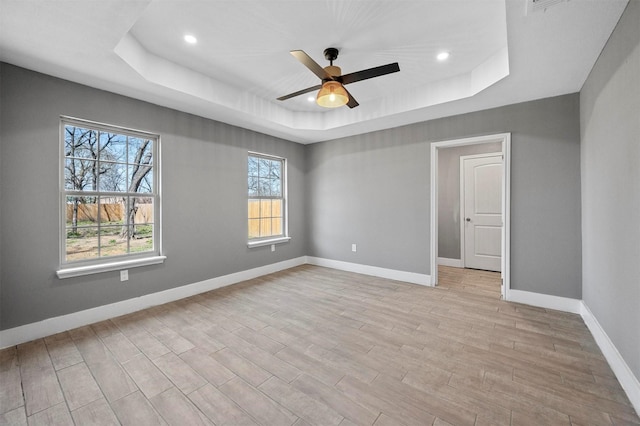 unfurnished bedroom featuring light wood finished floors, recessed lighting, a raised ceiling, and baseboards