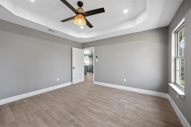 unfurnished room with a tray ceiling, visible vents, light wood-style flooring, and baseboards