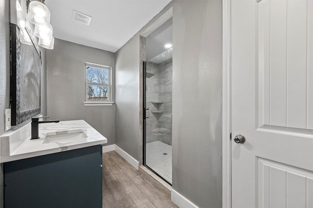 full bath with visible vents, baseboards, vanity, a shower stall, and wood finish floors