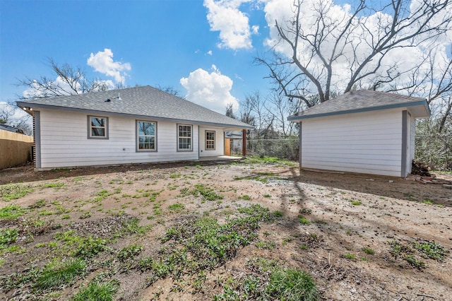 back of property featuring a shingled roof, an outbuilding, and fence