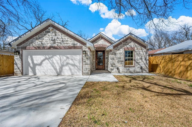 french country style house featuring an attached garage, stone siding, fence, and concrete driveway