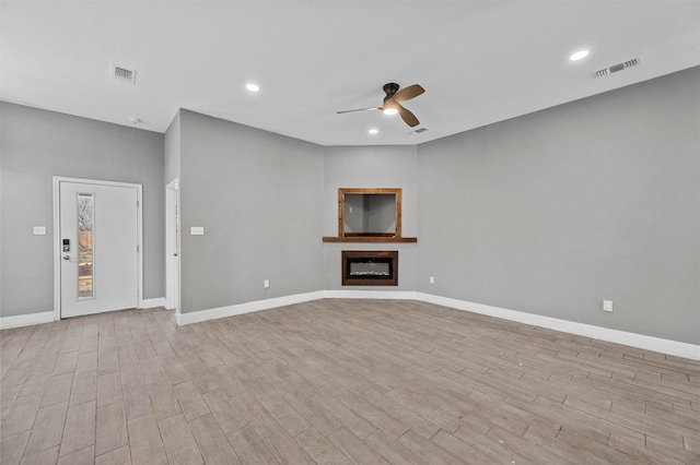 unfurnished living room featuring a glass covered fireplace, visible vents, baseboards, and wood finished floors