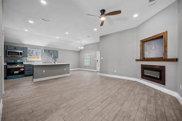 kitchen featuring stainless steel appliances, visible vents, open floor plan, light countertops, and a glass covered fireplace