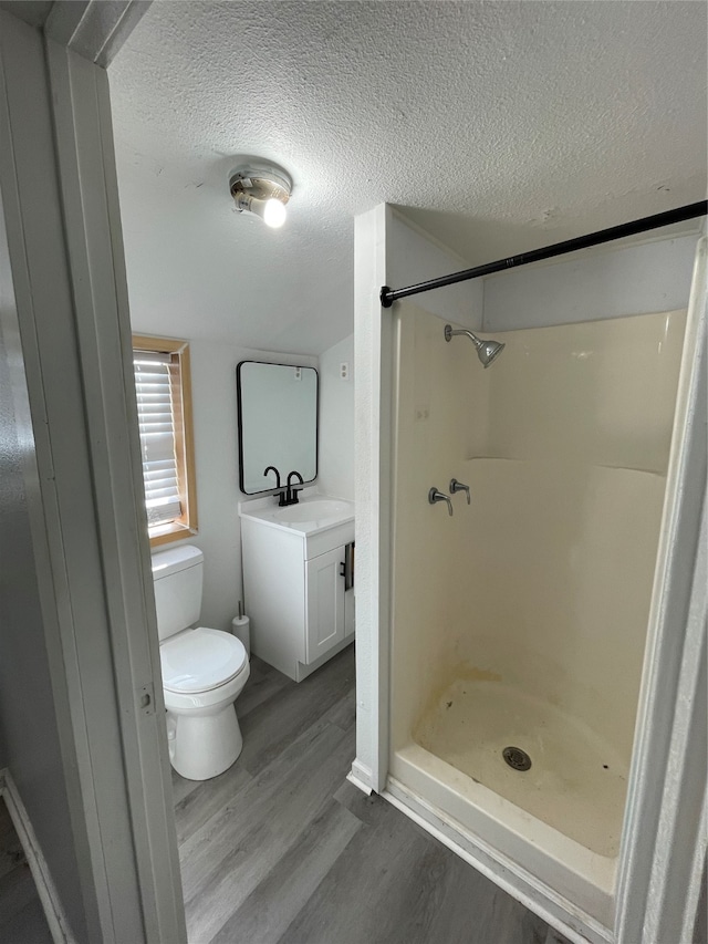 bathroom with a textured ceiling, hardwood / wood-style flooring, a shower, toilet, and vanity