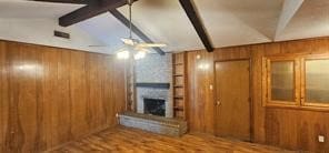 unfurnished living room featuring vaulted ceiling with beams, a large fireplace, light wood-type flooring, and wooden walls