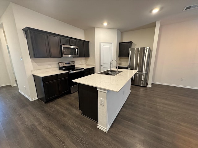 kitchen with dark hardwood / wood-style floors, sink, a kitchen island with sink, light stone countertops, and stainless steel appliances