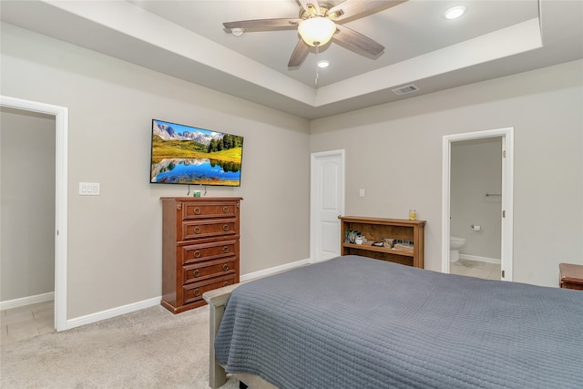 carpeted bedroom featuring ceiling fan, ensuite bath, and a tray ceiling