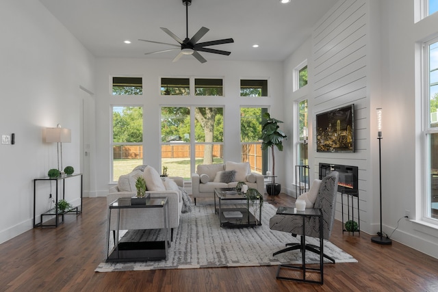 living room featuring a high ceiling, a fireplace, a wealth of natural light, and dark wood-type flooring