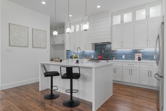 kitchen with white cabinets, stainless steel refrigerator, a kitchen island with sink, and dark wood-type flooring