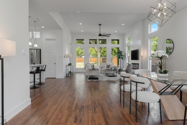 living room with ceiling fan with notable chandelier, dark wood-type flooring, and a high ceiling