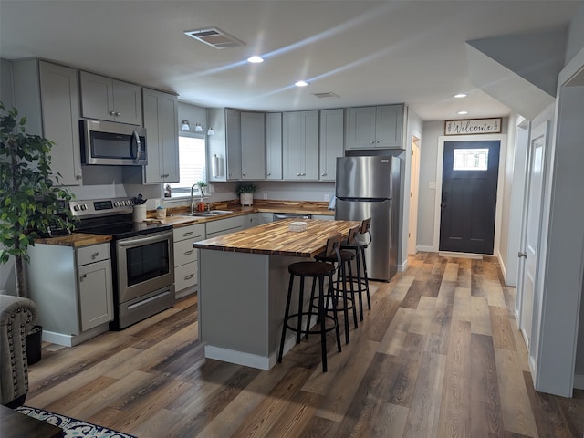 kitchen featuring hardwood / wood-style floors, a center island, stainless steel appliances, sink, and butcher block countertops