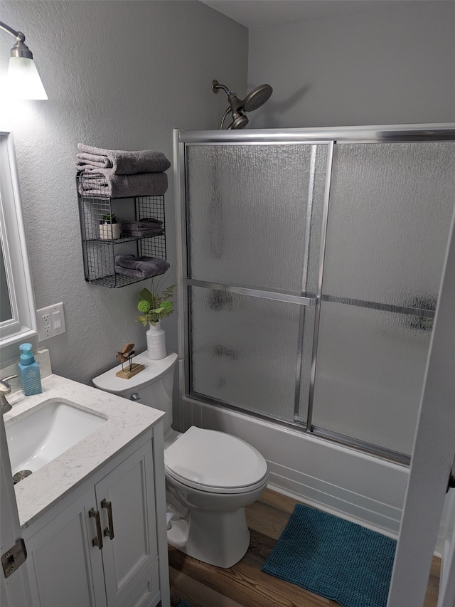 full bathroom with toilet, vanity, wood-type flooring, and combined bath / shower with glass door