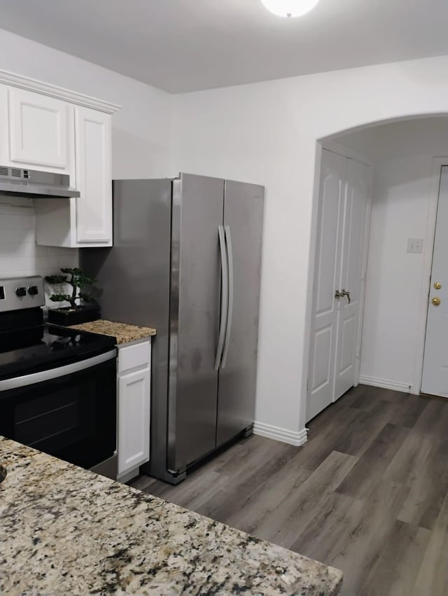 kitchen featuring light stone counters, range hood, white cabinetry, appliances with stainless steel finishes, and dark wood-type flooring