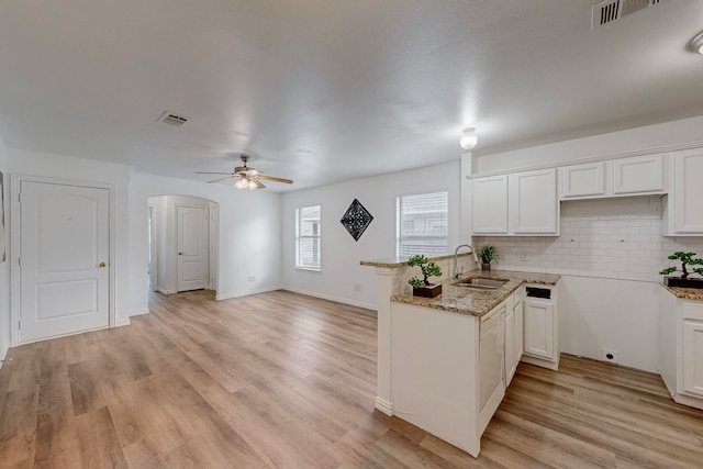 kitchen with sink, kitchen peninsula, backsplash, light hardwood / wood-style flooring, and white cabinets